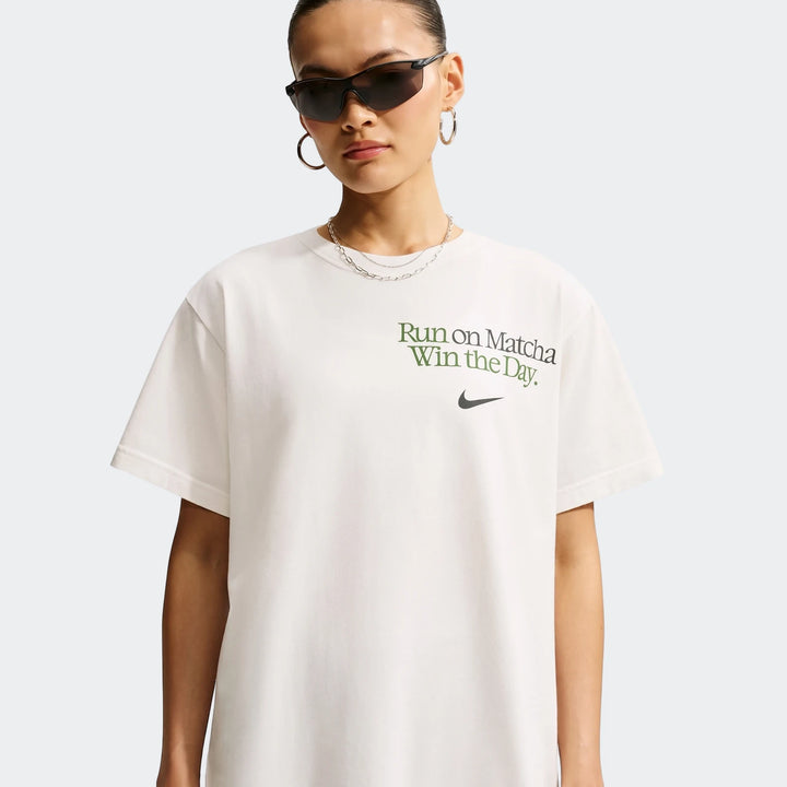 A woman wears a white Nike Sportswear oversized t-shirt featuring 'Run on Matcha Win the Day' text and a Nike swoosh logo.