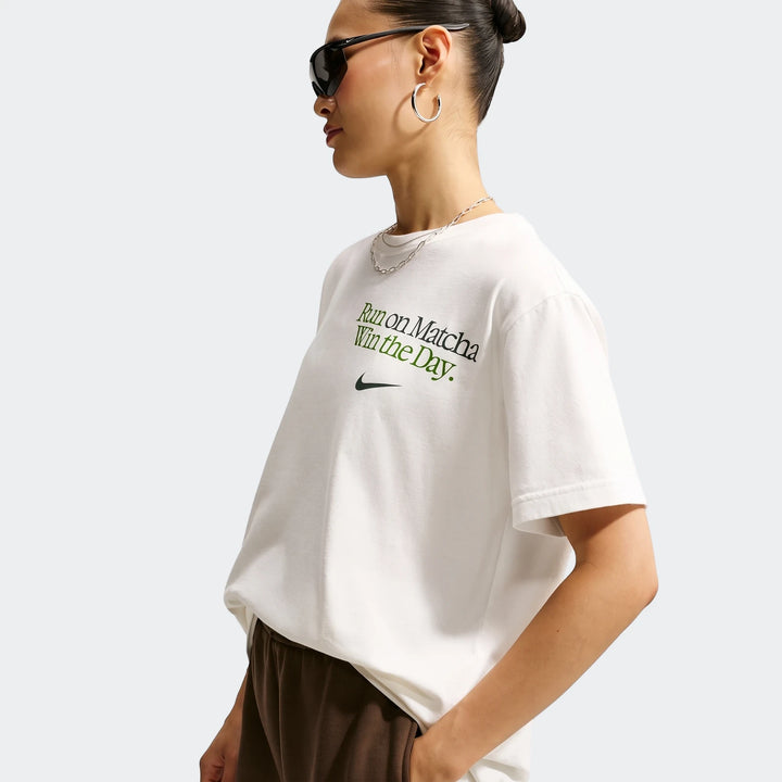 Nike Sportswear Women's Oversized T-shirt in white with green text and a black swoosh, worn by a model with sunglasses and