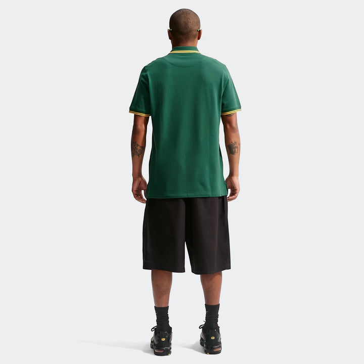 Back view of a man wearing a green Nike Springboks Pique Polo Golfer with gold trim, black shorts, and black sneakers.