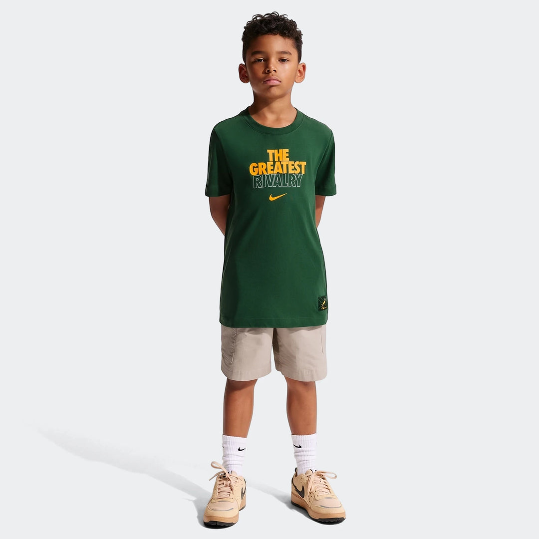 Young boy wearing a green Nike Springboks Rugby’s Greatest Rivalry Tour kids t-shirt, beige shorts, and sneakers.