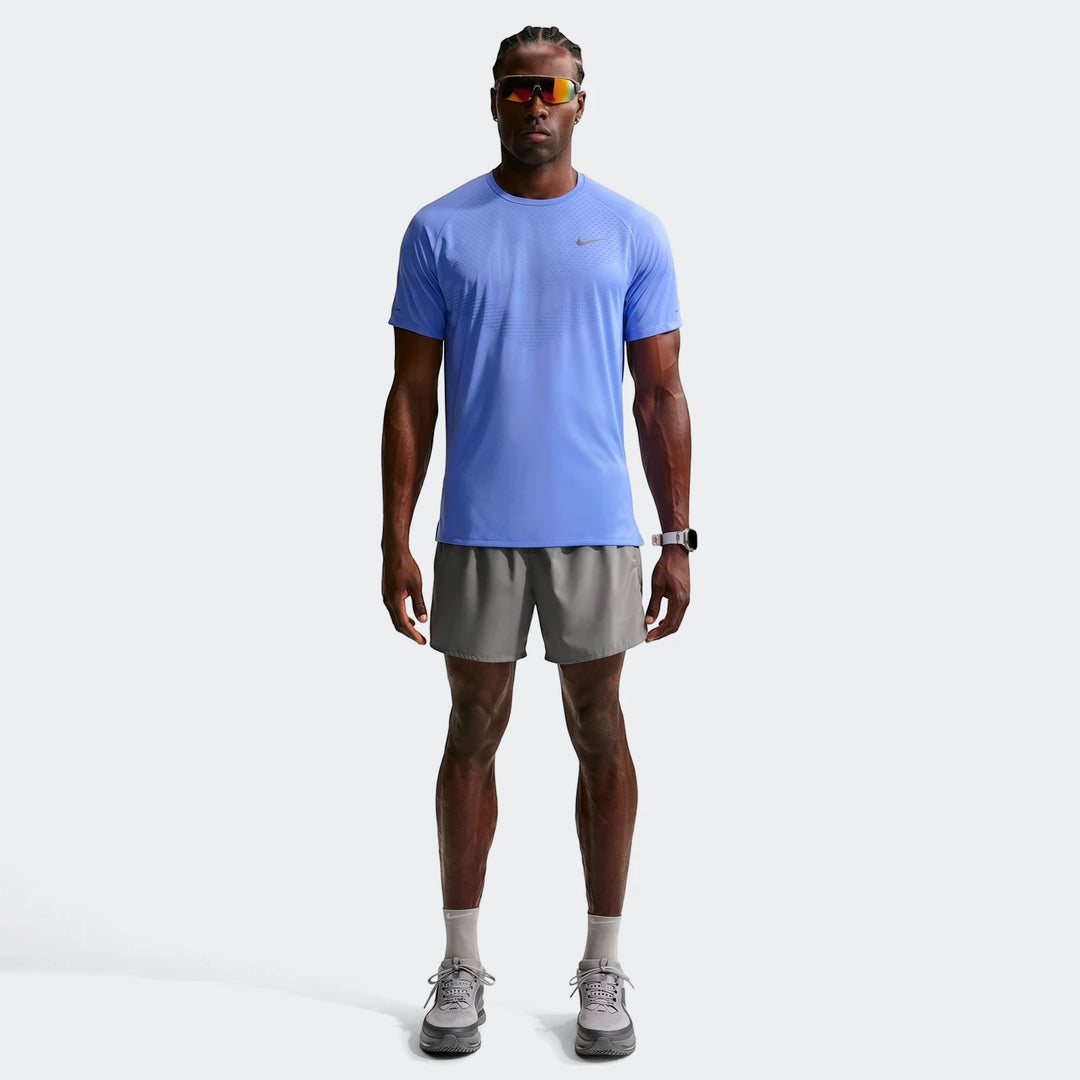 Full body shot of a man wearing a blue Nike Stride Dri-Fit ADV short-sleeve running top and grey shorts, looking forward.