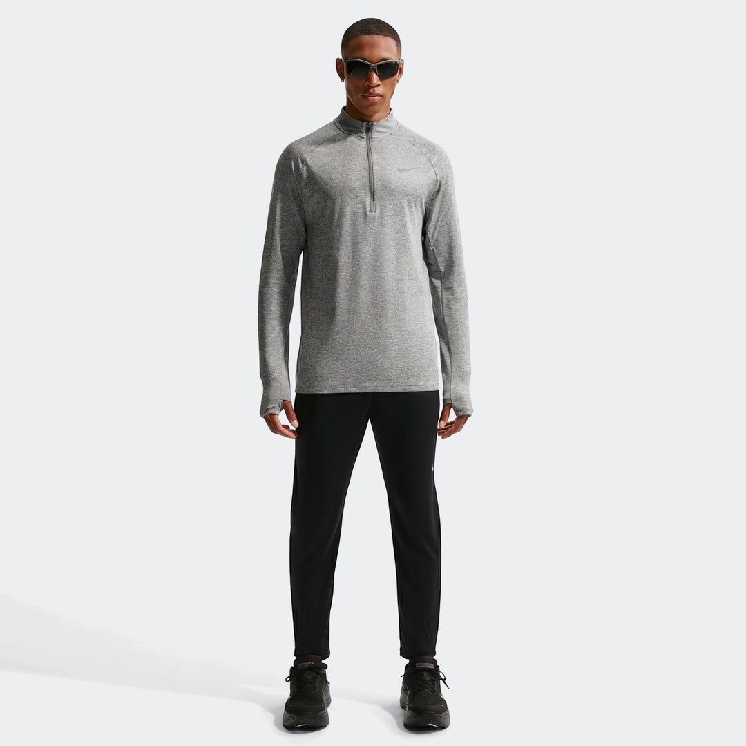 A man models a grey Nike Stride Dri-Fit 1/4-Zip Running Top with black athletic pants and shoes.