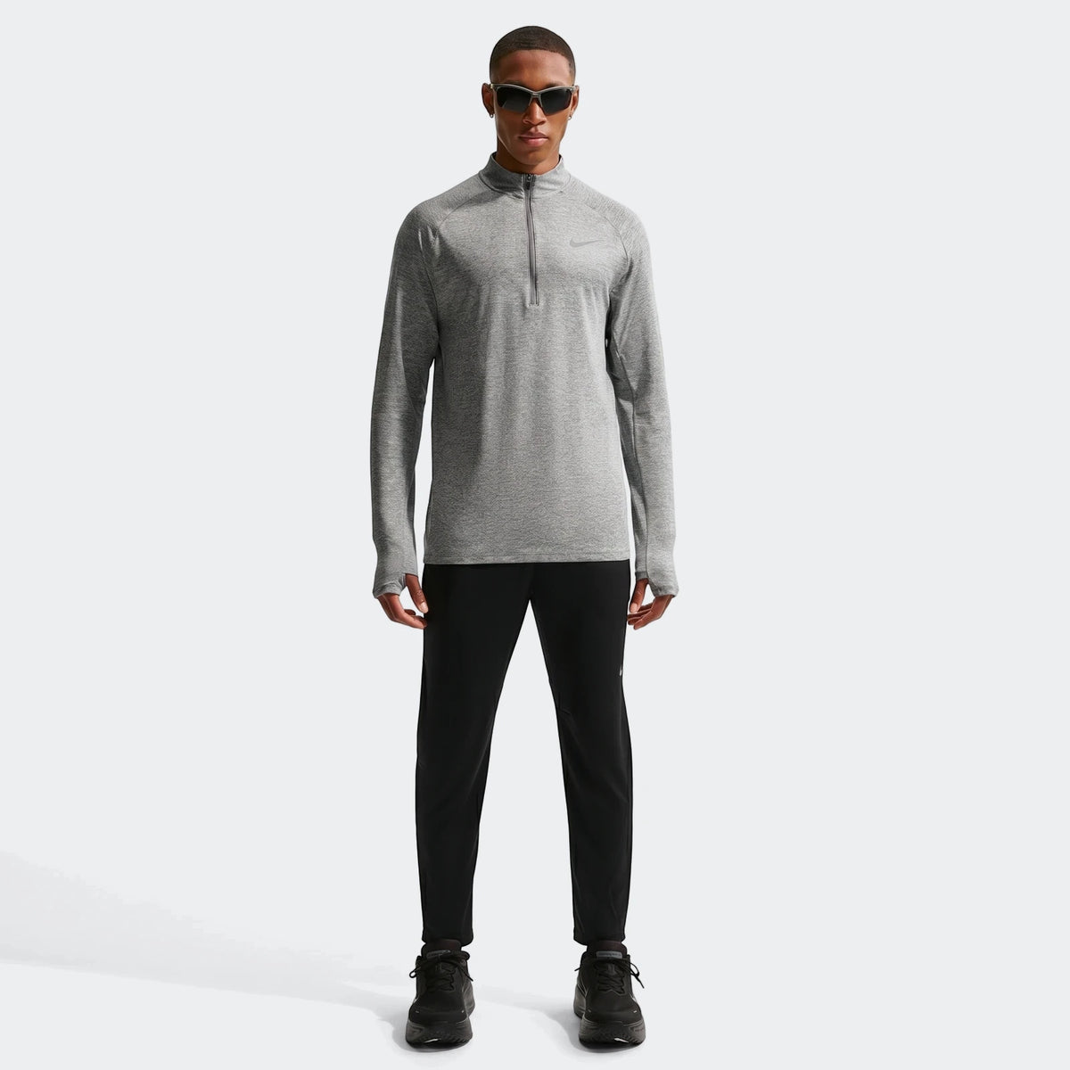 A man models a grey Nike Stride Dri-Fit 1/4-Zip Running Top with black athletic pants and shoes.