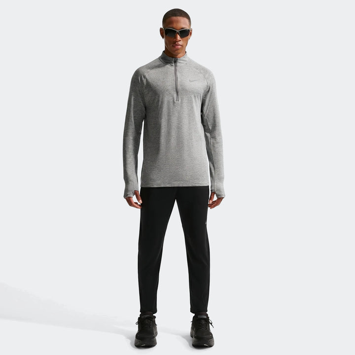 A man models a grey Nike Stride Dri-Fit 1/4-Zip Running Top with black athletic pants and shoes.