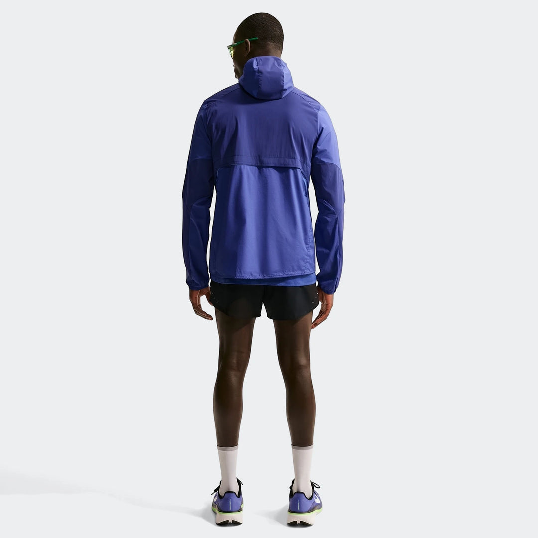 Rear view of a man wearing a blue Nike Stride Plus Repel running jacket, black shorts, and running shoes.