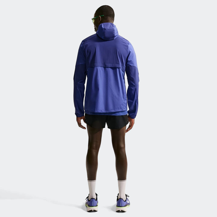 Rear view of a man wearing a blue Nike Stride Plus Repel running jacket, black shorts, and running shoes.