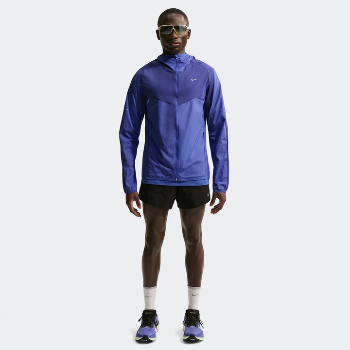 Full body shot of a man wearing a Nike Stride Plus Blue Men's Repel Running Jacket, black running shorts, and purple running