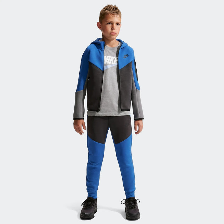 Young boy wearing a Nike Tech Fleece blue, gray, and black hoodie, matching sweatpants, and a gray Nike t-shirt, posing