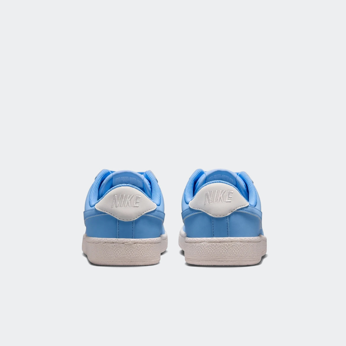 Pair of Nike Tennis Classic Big Kids' shoes in light blue and white, seen from the back view, showcasing the heel logos and