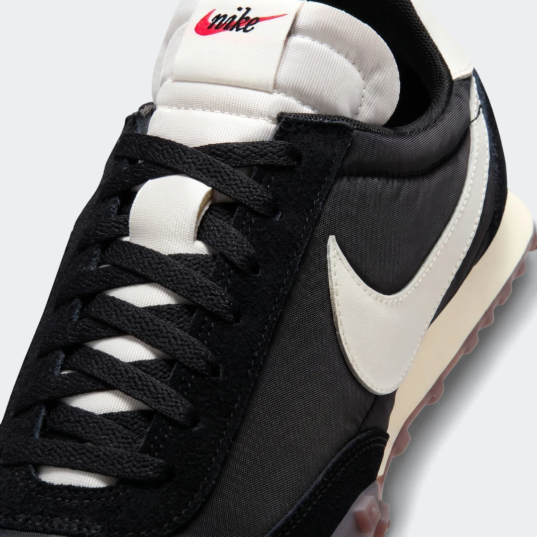 Close-up of a Nike Waffle Racer men's shoe in black and white with a red logo on the tongue.