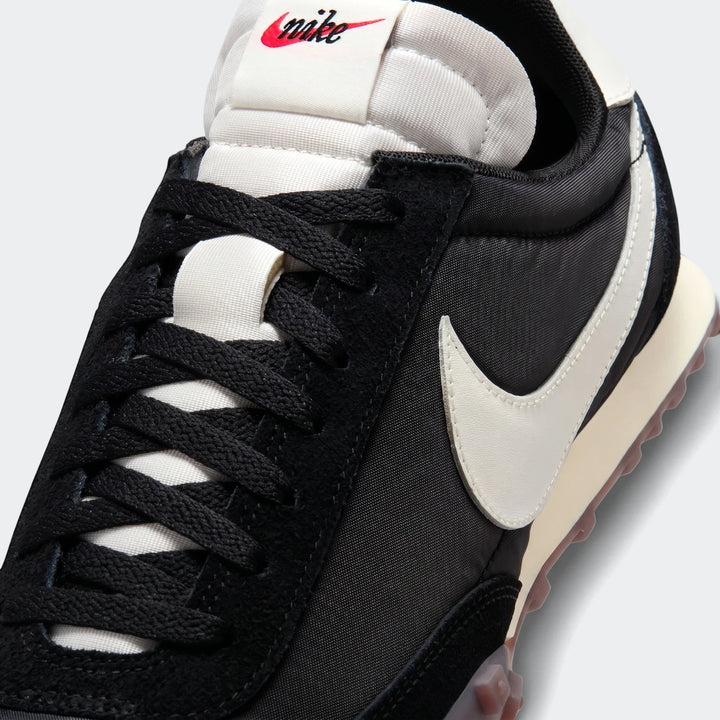 Close-up of a Nike Waffle Racer men's shoe in black and white with a red logo on the tongue.