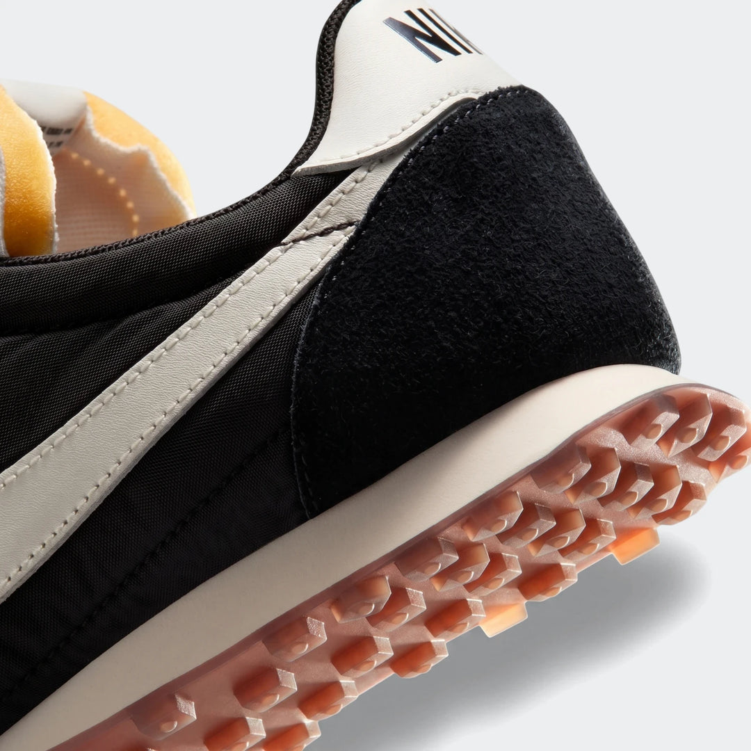 Close-up of a Nike Waffle Racer men's shoe, featuring a black upper with white swoosh and waffle outsole.