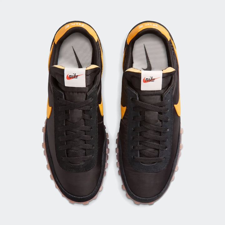 Top-down view of black and orange Nike Waffle Racer men's shoes featuring black laces, yellow swooshes, and a rugged waffle