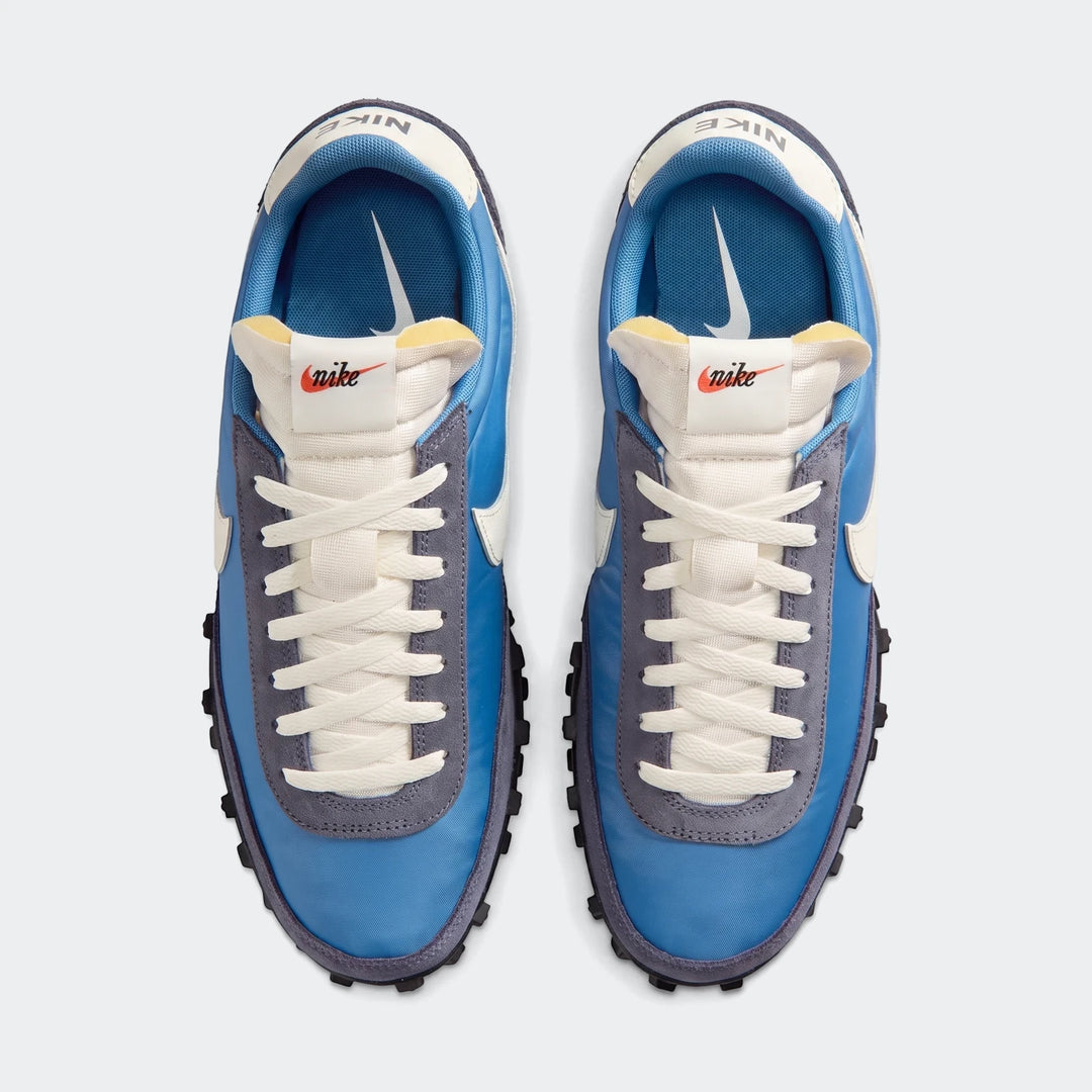 Top-down view of men's blue and gray Nike Waffle Racer shoes with cream white laces on a white studio background.