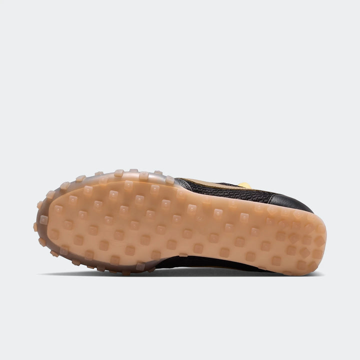 Bottom view of a black and gold Nike Waffle Racer Se men's shoe with a translucent tan waffle rubber sole.