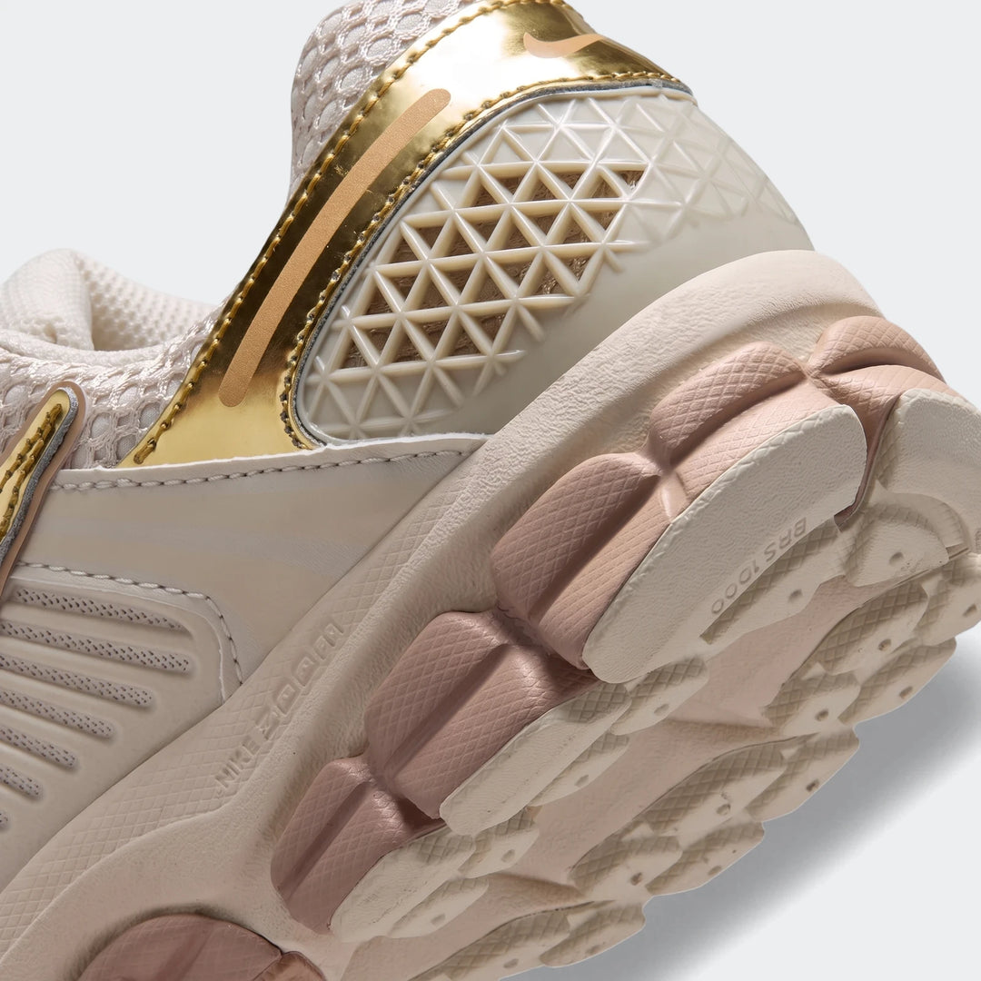 Close-up of a beige and gold Nike Zoom Vomero 5 women's running shoe, highlighting the intricate sole and heel details.