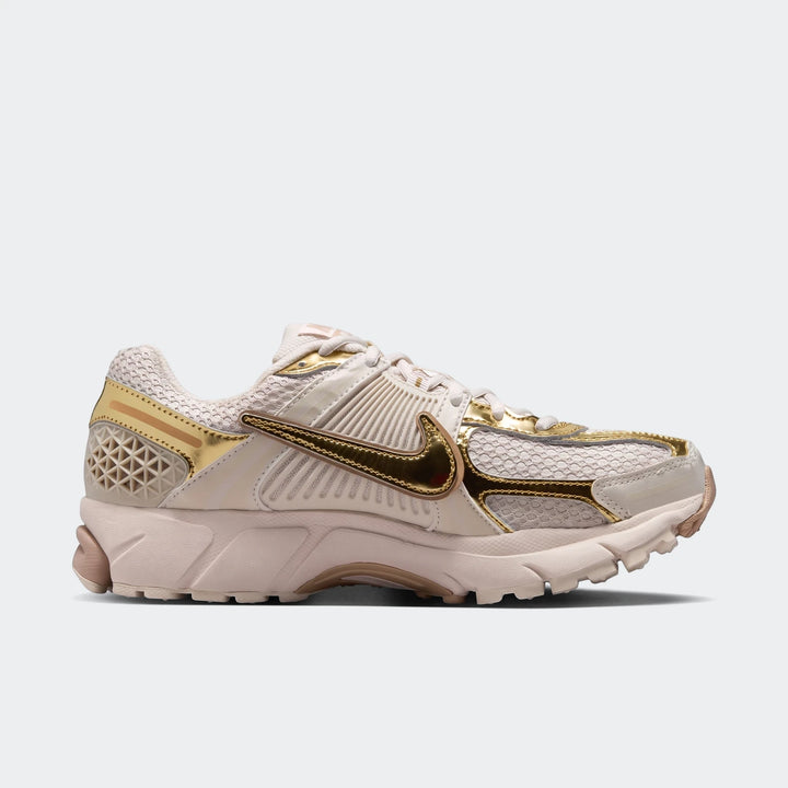 Side view of Nike Zoom Vomero 5 women's running shoes in cream and metallic gold, featuring mesh panels and a prominent