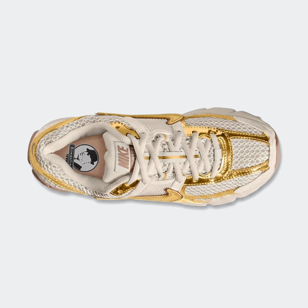 Top-down view of a Nike Zoom Vomero 5 Women's shoe in beige and metallic gold, featuring mesh and synthetic overlays.