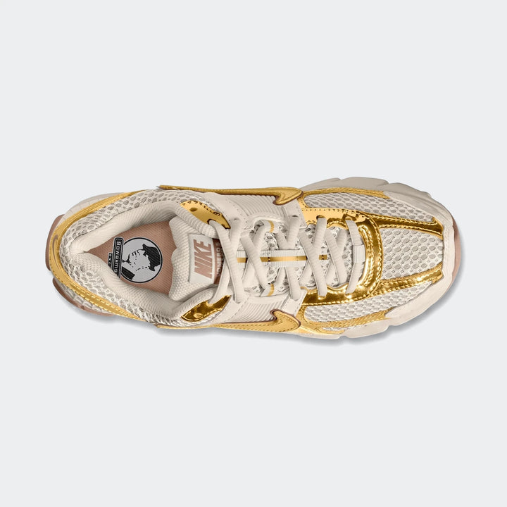 Top-down view of a Nike Zoom Vomero 5 Women's shoe in beige and metallic gold, featuring mesh and synthetic overlays.
