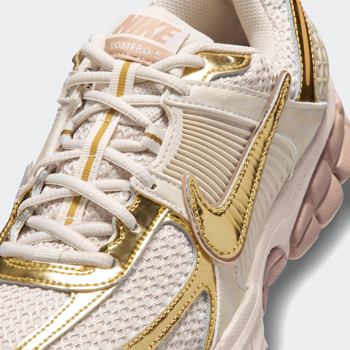 Close-up of a cream and metallic gold Nike Zoom Vomero 5 Women's shoe, showcasing its detailed upper.