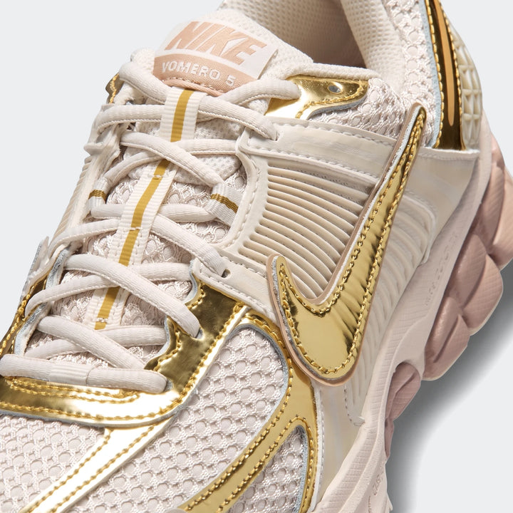 Close-up of a cream and metallic gold Nike Zoom Vomero 5 Women's shoe, showcasing its detailed upper.