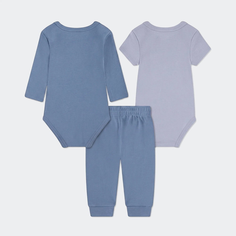 Nkn Essentials 3-piece baby set with blue long-sleeve bodysuit, light blue short-sleeve bodysuit, and blue pants, flat lay.