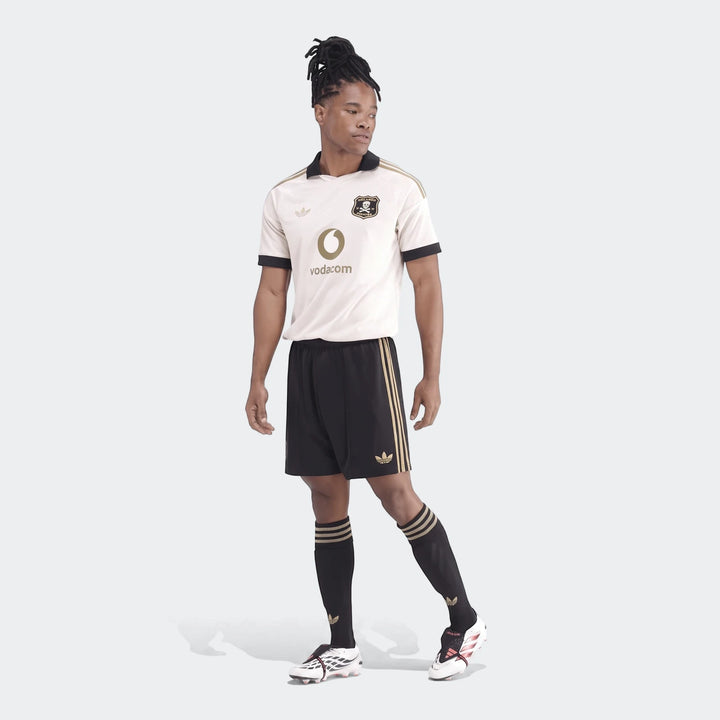 Male model wearing an Op A Sho white and black soccer jersey kit, featuring black shorts with gold stripes and white cleats.