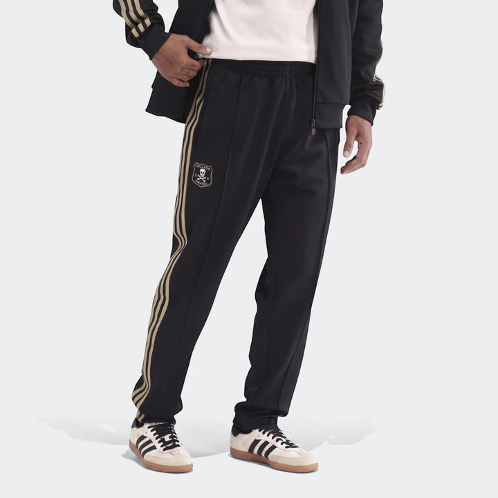 Black and gold Op Og2 Tp track pants, featuring the Orlando Pirates logo, paired with cream Adidas Samba sneakers.
