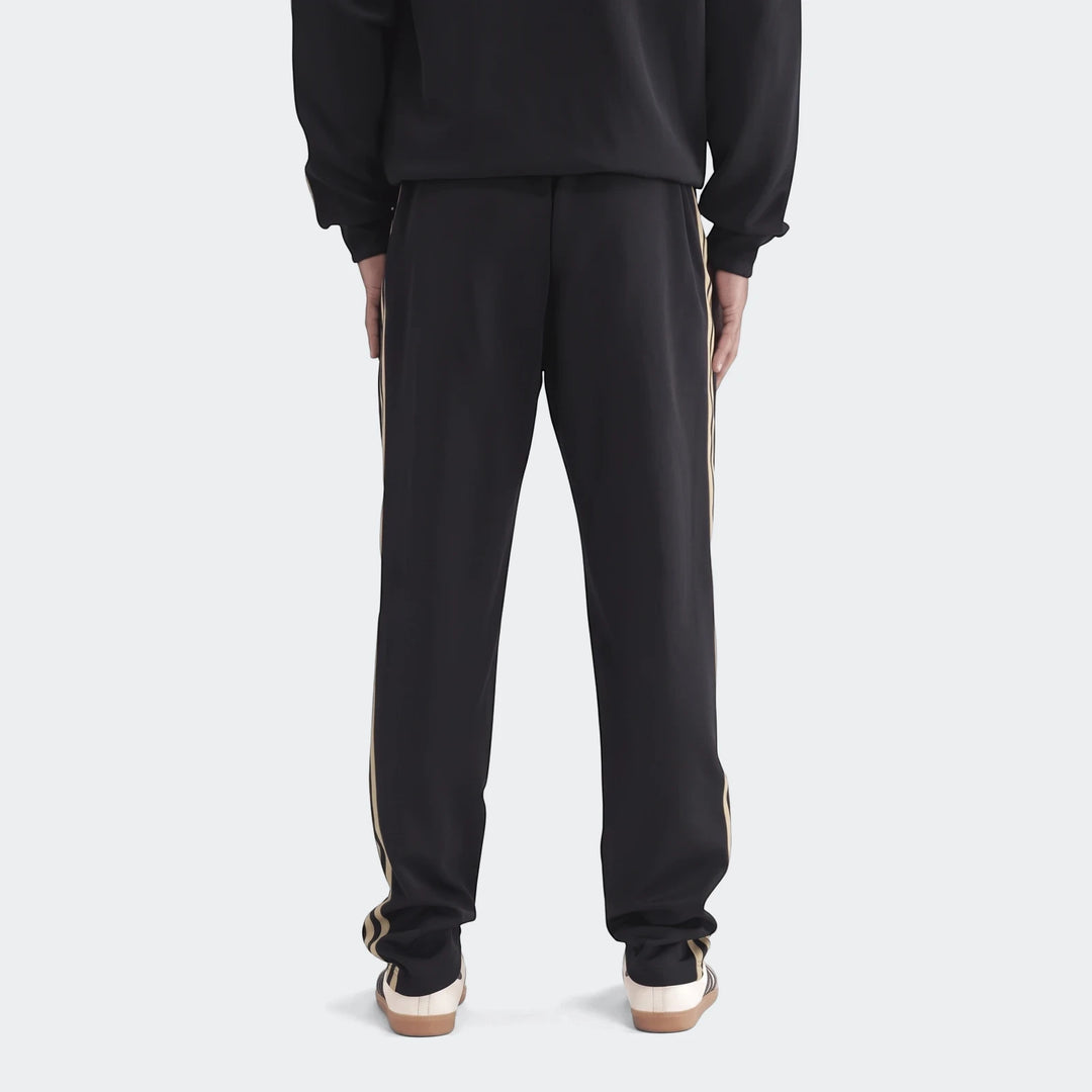 Op Og2 Tp black sweatpants with gold side stripes, worn by a person standing with their back to the camera, full length.
