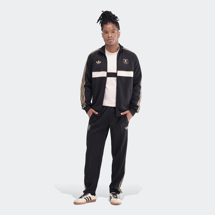 Male model wearing an Op Og2 Tp black and gold Adidas tracksuit with white accents and classic Adidas Samba sneakers.