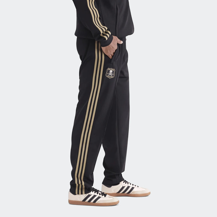 Op Og2 Tp men's black track pants with gold stripes and Orlando Pirates logo, paired with cream and black sneakers, side