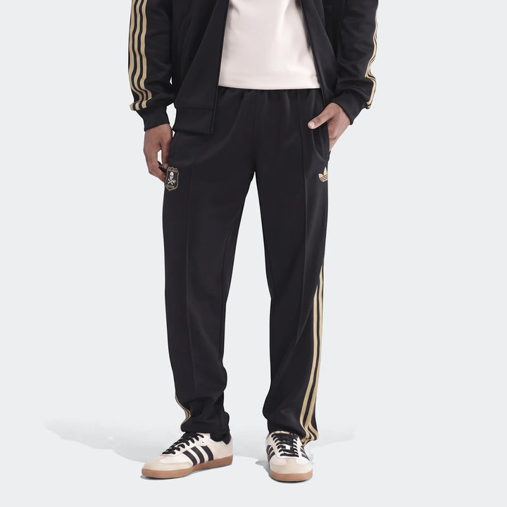Op Og2 Tp men's black tracksuit pants with gold stripes, an Adidas logo, and Orlando Pirates FC crest worn by a model.