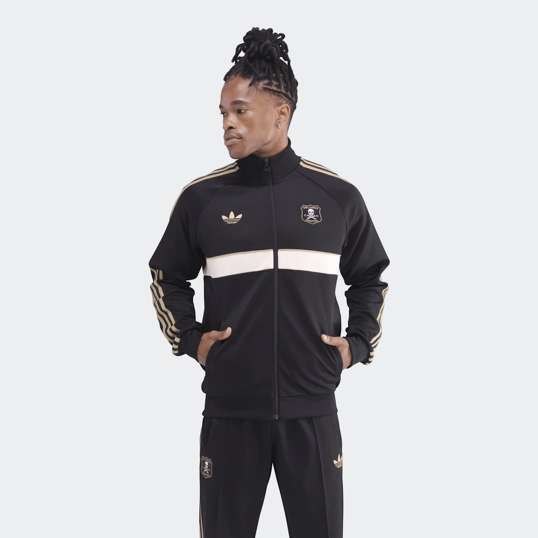 Male model wearing a black and gold Adidas Op Og2 Tt track jacket and matching pants, standing with hands in pockets.