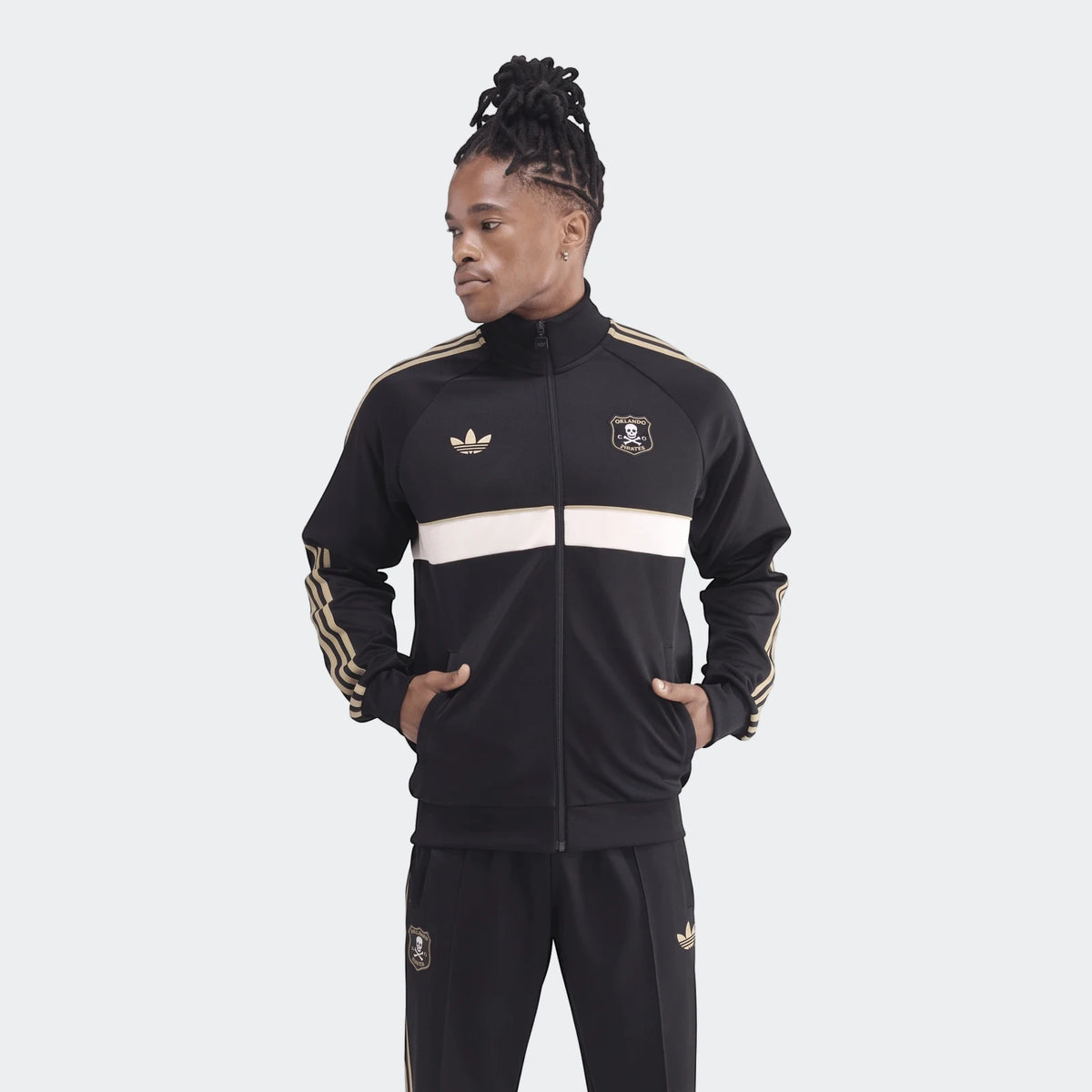 Male model wearing a black and gold Adidas Op Og2 Tt track jacket and matching pants, standing with hands in pockets.