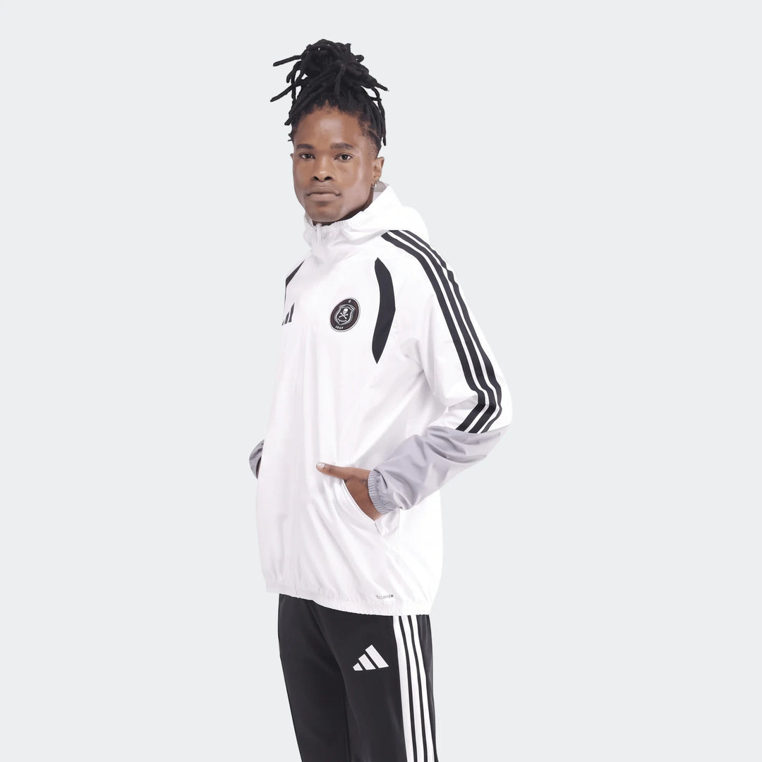 Male model wearing a white and black Adidas Op Tiro26C Aw Jkt, standing with hands in pockets.