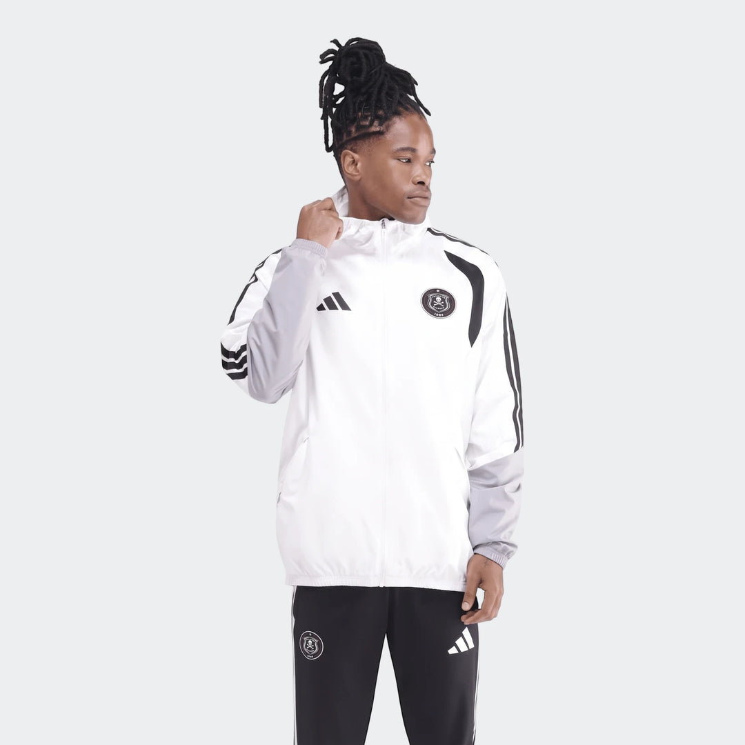 Male model wearing a white, grey, and black Adidas Op Tiro26C Aw Jkt with Orlando Pirates branding, paired with matching
