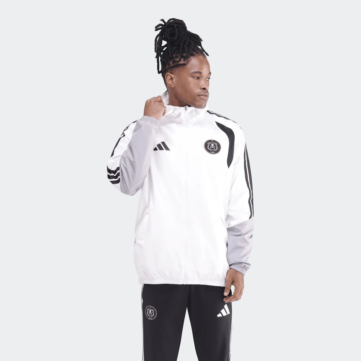 Male model wearing a white, grey, and black Adidas Op Tiro26C Aw Jkt with Orlando Pirates branding, paired with matching