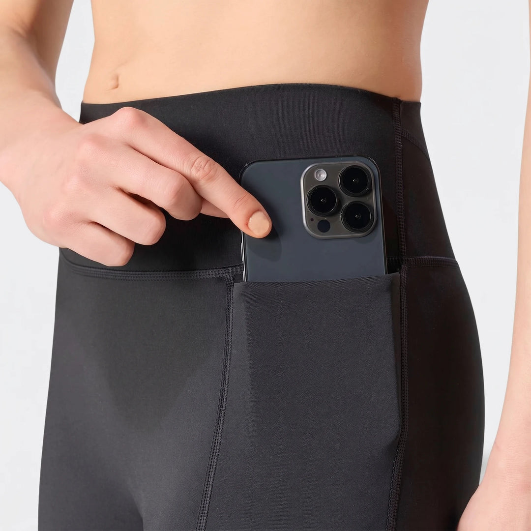 Close-up of black Optime Workout Contour Full Length Leggings, showing a model's hand inserting a smartphone into the side
