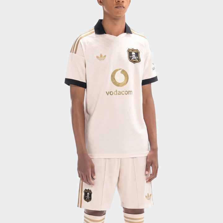 Male model wearing an Orlando Pirates 26/27 Away Kit, featuring beige jersey and shorts with gold Adidas logos and team