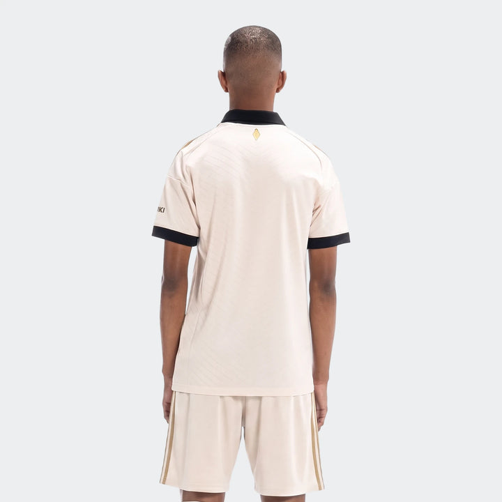 Orlando Pirates 26/27 Away Jersey in beige, featuring black collar and cuffs, with gold details, viewed from the back on a