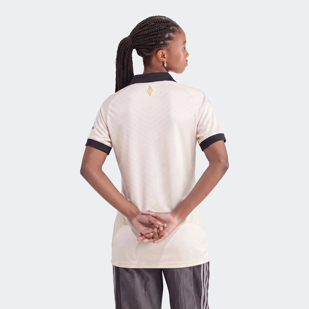 Back view of a woman wearing an Orlando Pirates 26/27 Away Jersey in beige with black details and a subtle pattern.