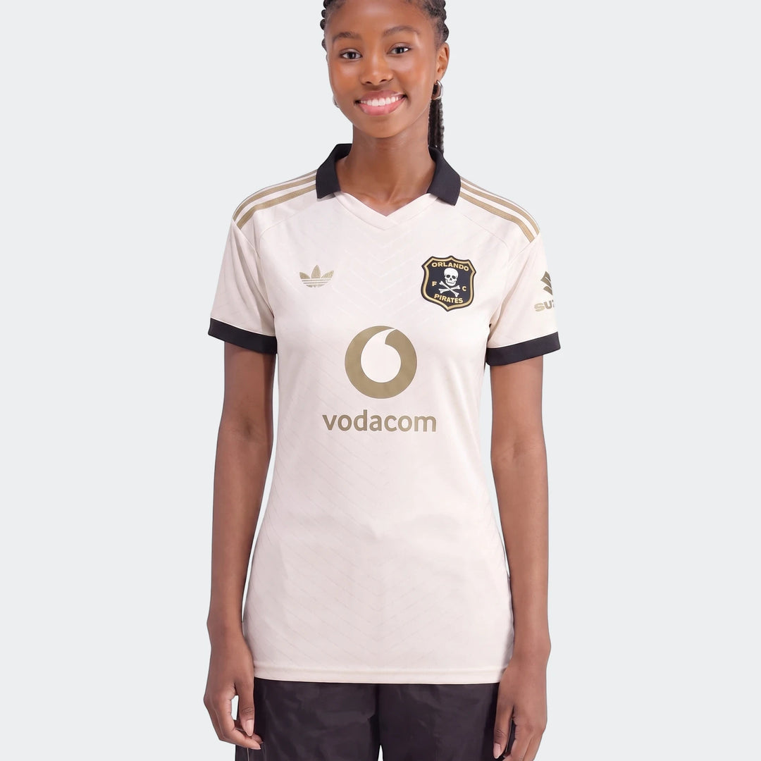 Front view of a smiling female model wearing the cream and gold Orlando Pirates 26/27 Away Jersey with sponsor logos.