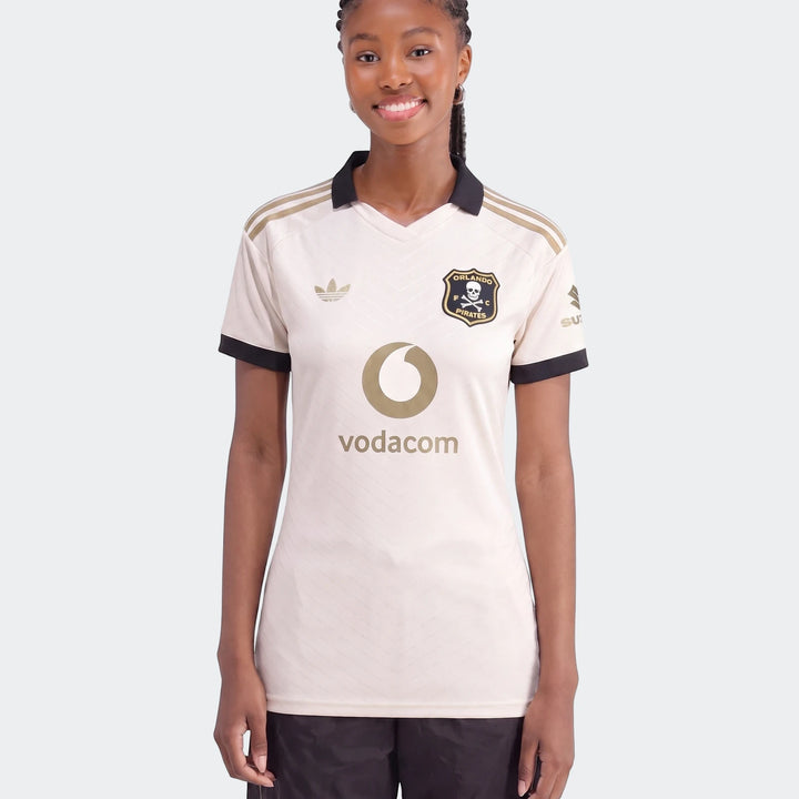 Front view of a smiling female model wearing the cream and gold Orlando Pirates 26/27 Away Jersey with sponsor logos.