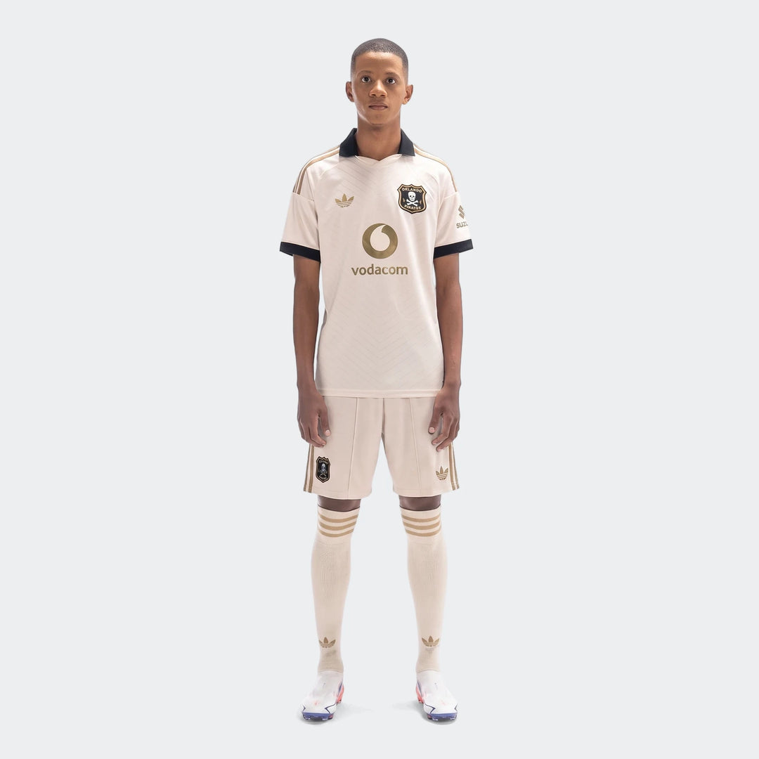 Male model wearing Orlando Pirates 26/27 Away Shorts in beige, paired with a matching jersey and socks, standing full-length.