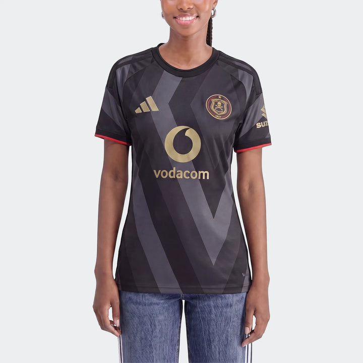 Female model wearing an Orlando Pirates 26/27 Home Jersey, featuring black and gray chevron patterns with gold logos and red