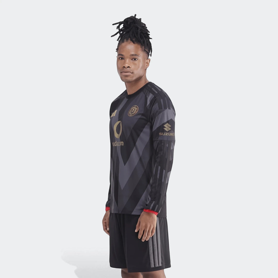Male model wearing an Orlando Pirates 26/27 Home Jersey, black and gray long-sleeve, featuring gold logos and details.