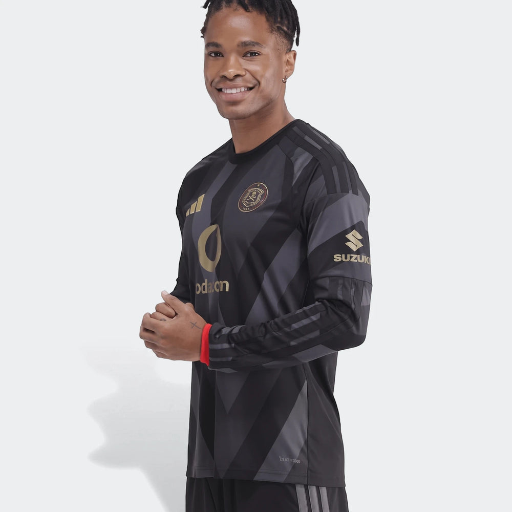 Smiling man in a black Orlando Pirates 26/27 Home Jersey with long sleeves, featuring dark gray patterns and gold logos.