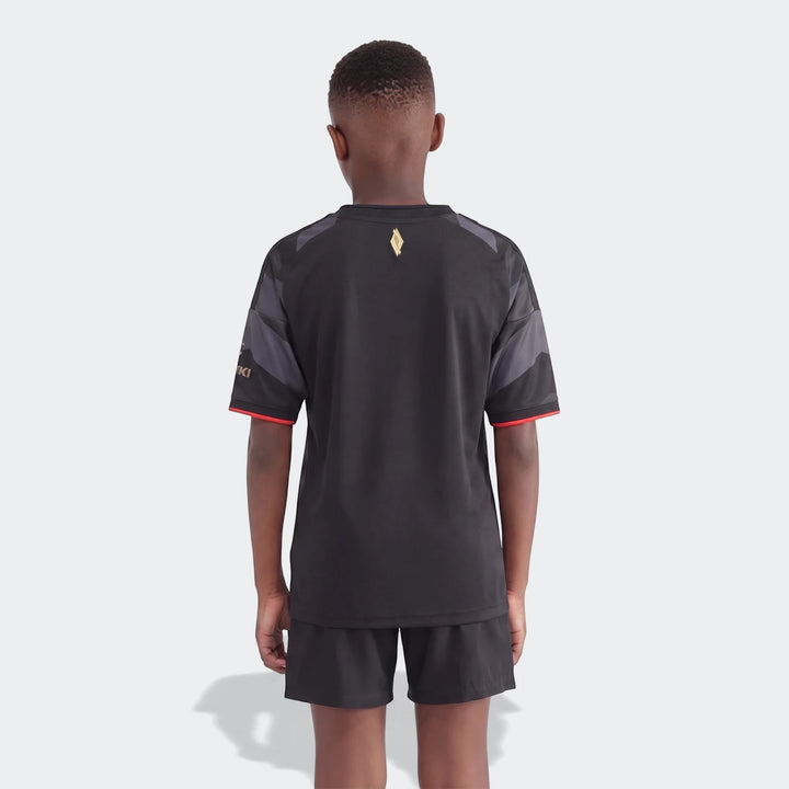 Back view of a young boy wearing an Orlando Pirates 26/27 Home Kids Jersey, featuring black, gray, and red design with a