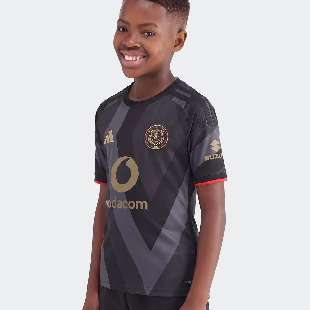 Young boy smiling while wearing an Orlando Pirates 26/27 Home Jersey in black and grey with geometric patterns and gold