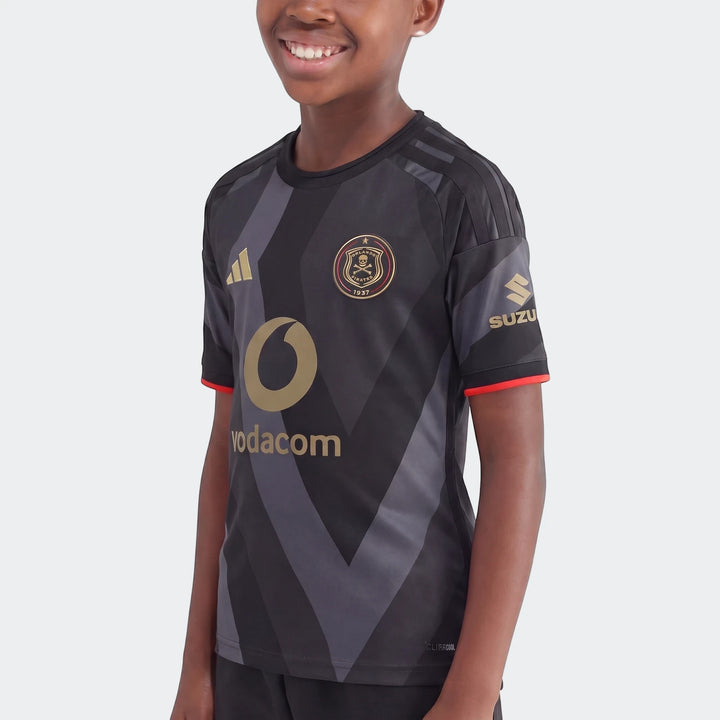 A young boy smiles while wearing the black and grey Orlando Pirates 26/27 Home Jersey for kids, featuring gold Adidas,